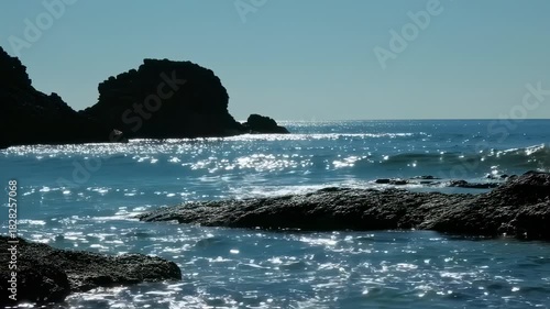 Ocean scene with silhouetted rocks, shimmering water, and a bright sky
