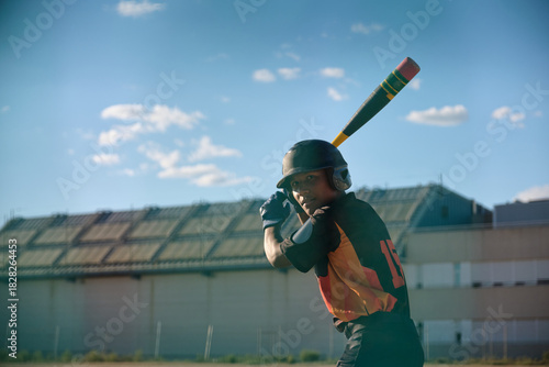 Teenager in uniform ready to bat while playing baseball under a clear sky