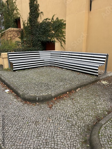 Berlin Germany October 2025 Graphic black and white corner bench on cobblestone patio by ochre wall