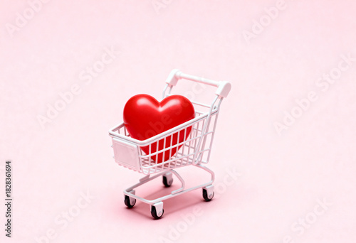 Red heart in mini shopping cart on a pastel pink background symbolizing love shopping and special offers for holiday
