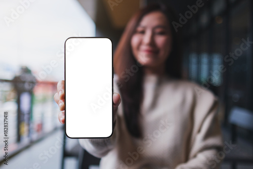 Mockup image of a woman holding and showing at a mobile phone with blank white screen