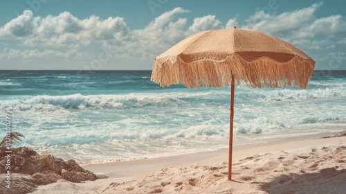 A straw umbrella stands on a sandy beach providing shade as sunlight sparkles on gentle ocean waves. The scene captures a peaceful day by the shore ideal for relaxation.