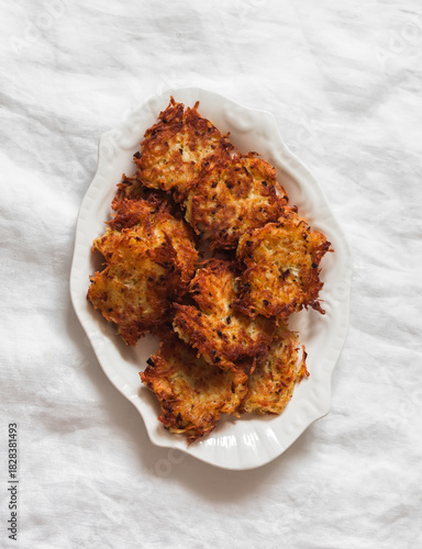 Crispy latkes potatoes on a white plate on a light background, top view
