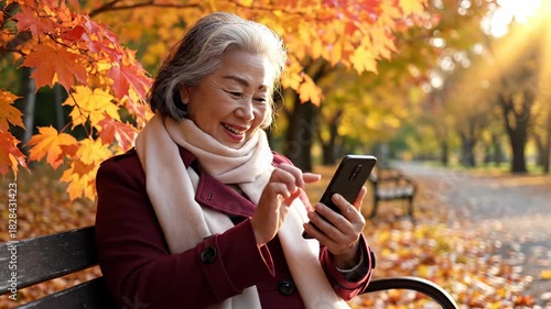 Senior woman smiles while using her smartphone on a park bench amid vibrant autumn foliage in soft, golden sunlight
