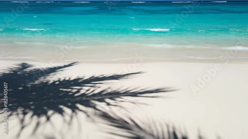 Serene beach view with turquoise water, soft waves, and palm frond shadows on white sand
