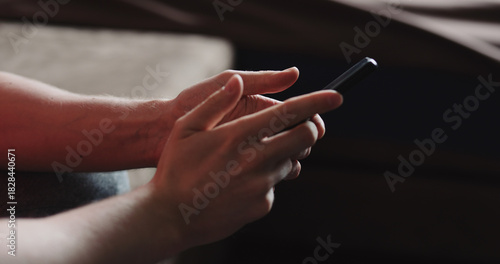 Closeup young man in black t-shirt typing messages on smartphone working from home side view
