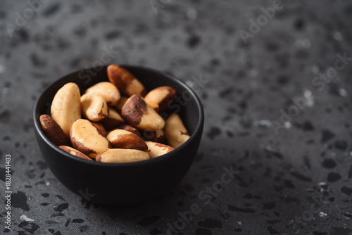 brazil nuts in black bowl on concrete background with copy space