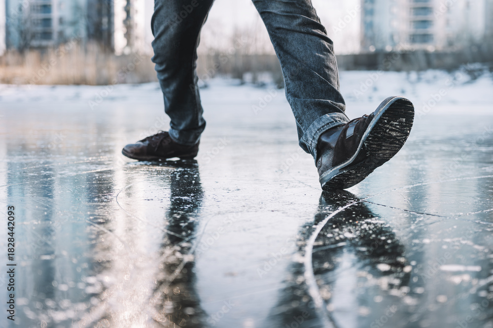 Naklejka premium Boots standing on icy ground, illustrating the danger of slipping on a frozen, slippery winter surface. man walks cautiously along an icy street on a winter day for fear of slipping and falling.