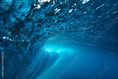 Underwater view breaking ocean wave tunnel deep blue barrel curling above, light filtering through translucent