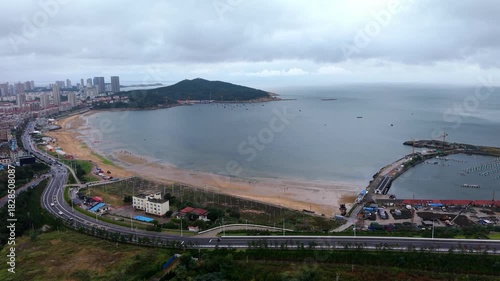 Curved golden sandy bay and fishing harbor with green hills, aerial China