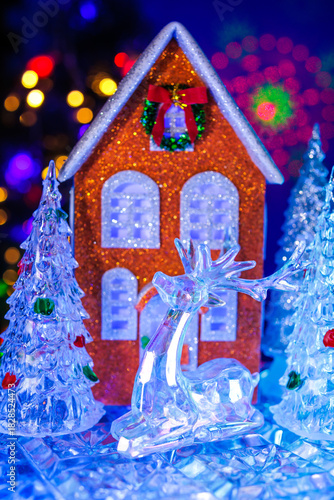 A close-up of glass Christmas trees around an orange house with a yellow car with a Christmas tree on the roof in front