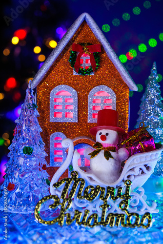 A close-up of glass Christmas trees with letters around the orange house and a snowman on a sled in front