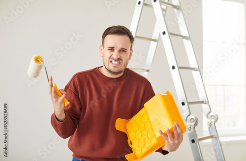 Angry male unprofessional painter or construction worker unable painting walls in white color with paint roller brush, problems with finishing task for room, building repair worry, not skilled