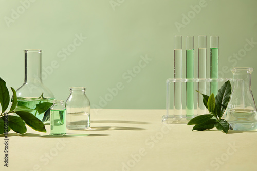 Tea leaves and clear beakers stand on a light green background, blending natural ingredients with a clean research aesthetic for skincare imaging. Space for design