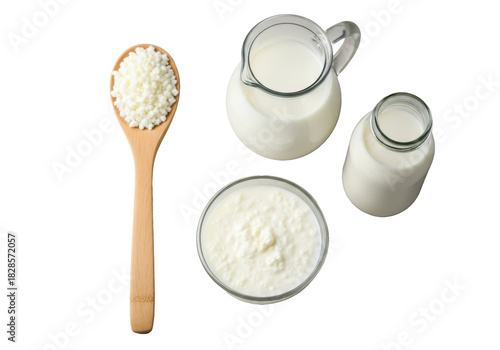 Wooden spoon with white kefir grains, glass bowl of homemade kefir, milk pitcher & bottle, on beige surface against transparent background, diffused light, concept of healthy probiotics