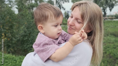 Mother holds funny one year old baby in her arms during a walk in the summer	
