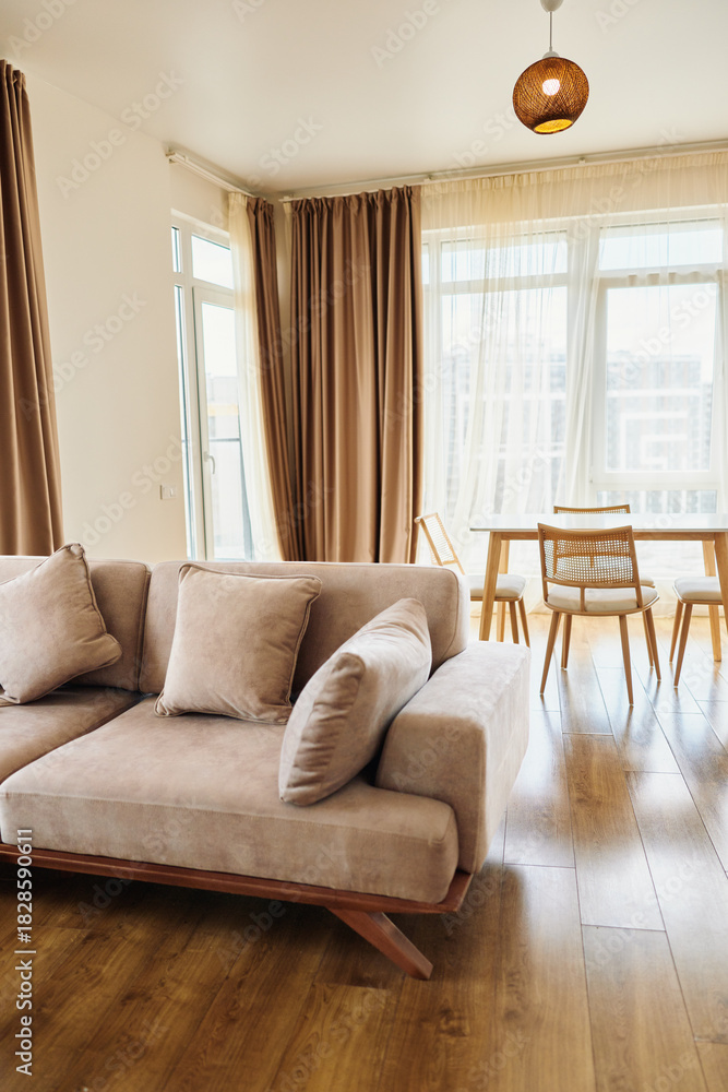 Naklejka premium Sofa pillows curtains table floor living home bright interior with modern beige couch and cozy cushions, large windows with sheer drapes and warm hardwood floors in open plan apartment