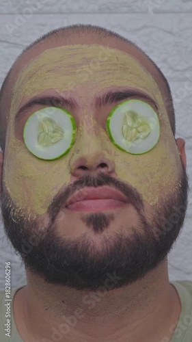 Vertical Video of Man Applying Cucumber on Eyes with Clay Mask on Face