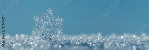 Delicate snowflake macro on glittering icy surface against clear blue sky, winter frost crystals closeup, minimalist seasonal background
