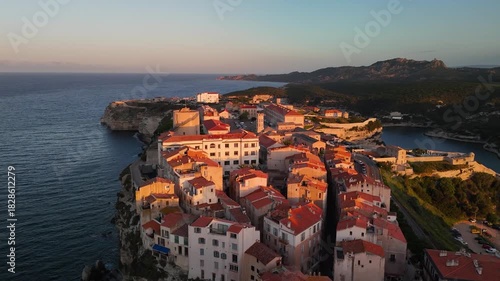 Expansive Aerial Drone Shot Reveals the Historic Bonifacio Citadel City Perched on Dramatic White Limestone Cliffs Above the Mediterranean Sea at Golden Hour Sunrise, Corsica, France.