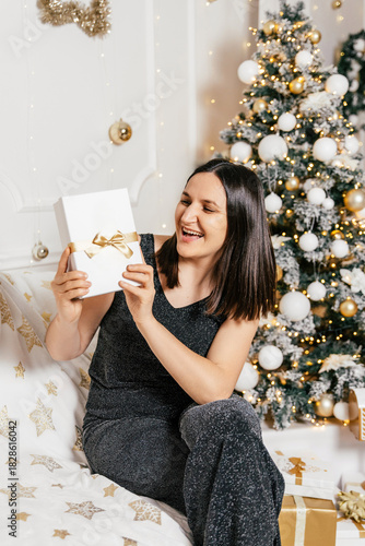 Woman joyfully opening a gift during festive holiday season at home with decorated Christmas tree