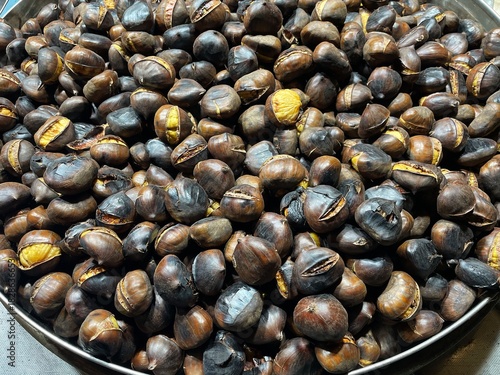 close-up photo of a pile of roasted chestnuts: large chestnuts, also known as marroni, cooked in a large pan after being harvested in November in northern Italy