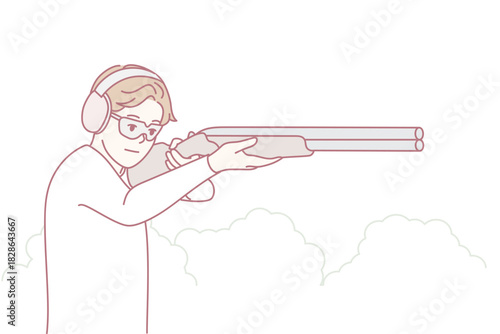 Target shooting focus, Serious shooter standing steady during outdoor clay shooting session, Depiction of focused shooter using headphones at outdoor shooting range concentrating on clay targets