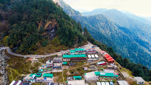 Aerial drone village town on cliff mountain edge with small concrete green red houses, narrow road and mountains in the distance in Chopta Tungnath uttarakhand India