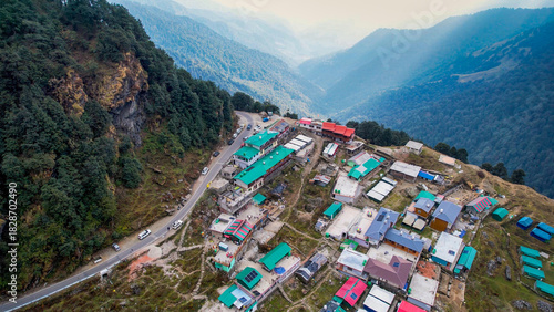 Aerial drone village town on cliff mountain edge with small concrete green red houses, narrow road and mountains in the distance in Chopta Tungnath uttarakhand India