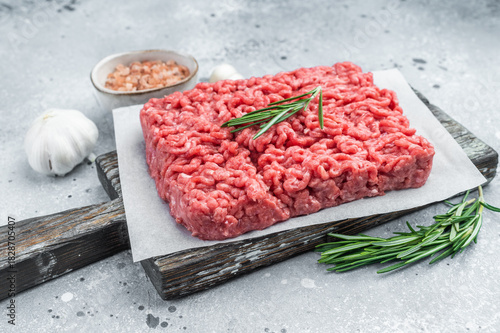 Cuadro en lienzo Fresh raw ground mince beef meat with rosemary on parchment over rustic wooden board and concrete background ideal for cooking and protein visuals