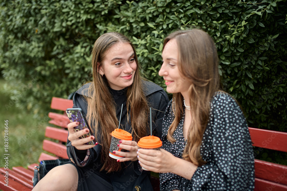 © TRAVELARIUM - Young adult girlfriends sharing gossip over coffee on park bench © TRAVELARIUM - Young adult girlfriends sharing gossip over coffee on park bench