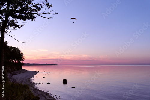 Fototapeta Naklejka Na Ścianę i Meble -  Tranquil Baltic Sea coastline at sunset with paraglider in sky