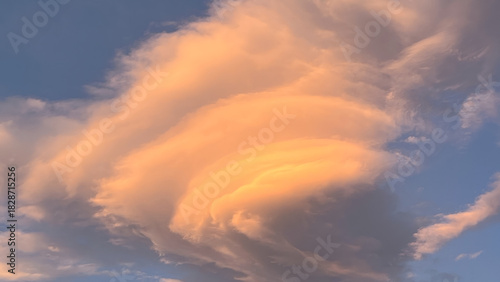 The beauty of a unique lenticular cloud formation against a blue sky. Cloud layers are illuminated with warm orange and pink sunlight during dawn in Wulai Taiwan.