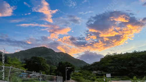 Dramatic sunrise or sunset sky over the silhouette of forested mountains and lush greenery in Wulai New Taipei City Taiwan. Clouds are brightly lit in orange and gold.