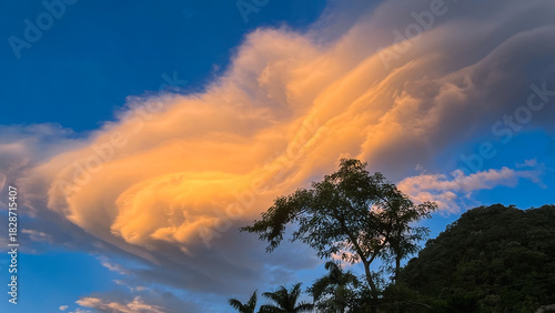Huge golden wave-shaped lenticular cloud at sunrise towering above trees in Wulai New Taipei City Taiwan.
