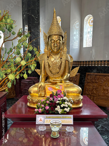 Golden Kakusandha Buddha statue inside Kek Lok Si Temple, Penang, Malaysia. Ornate Buddhist figure on a red altar with offerings. Symbolizes the first Buddha of the Bhadrakalpa.