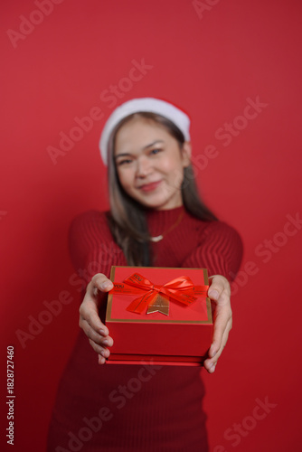 Xmas portrait of woman offering wrapped gift box – cheerful holiday mood, festive clothing and red color background for seasonal campaign