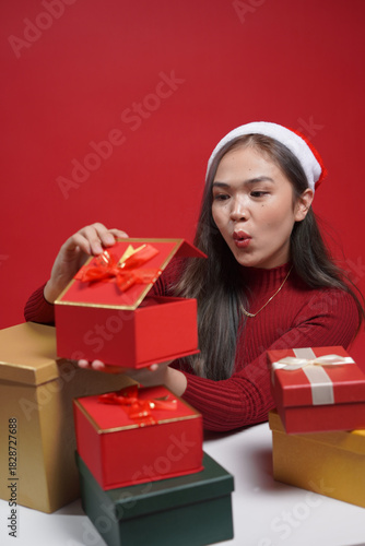 Christmas gift giving moment – beautiful woman in festive outfit holding wrapped box on red background, winter celebration and seasonal joy