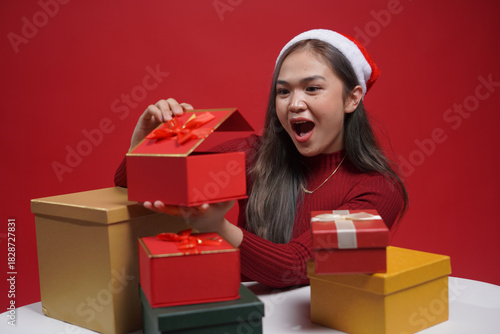 Holiday season portrait – young woman in Christmas costume offering gift box with smile, red studio background, perfect for festive promotions