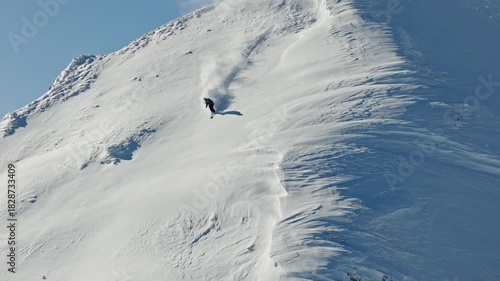 Aerial footage of a freeride skier carving through fresh powder snow on a steep alpine slope. Dynamic drone shot capturing the thrill of first tracks in pristine winter mountains.