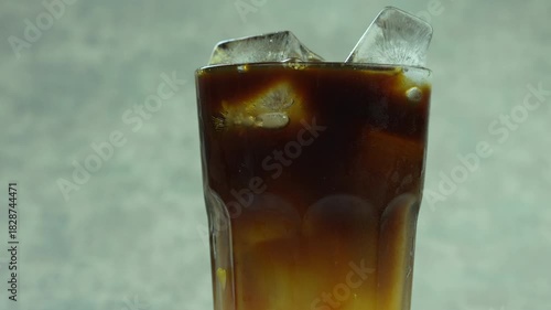 Rotates a glass of iced americano and fresh orange juice mix to glass, iced orange americano