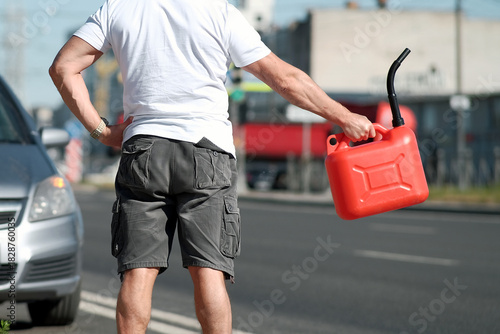 Stranded man signals for help, Driver in white shirt and grey shorts calls for assistance, Man with red fuel container flags passing vehicles while stranded near parked car