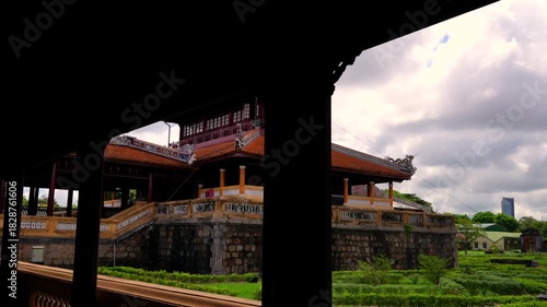 A wooden frame reveals the two-story Minh Lau Pavilion, perched on a rustic stone base amidst manicured geometric gardens