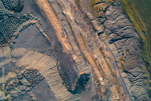 Fotografie Drone shot of textured, abstract patterns dark industrial tailings piles blending with multi-toned geological terraces
