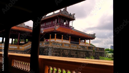 A wooden frame reveals the two-story Minh Lau Pavilion, perched on a rustic stone base amidst manicured geometric gardens