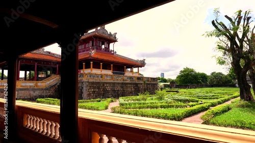 A wooden frame reveals the two-story Minh Lau Pavilion, perched on a rustic stone base amidst manicured geometric gardens