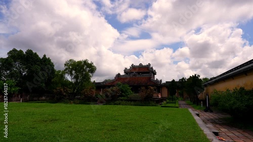 A wooden frame reveals the two-story Minh Lau Pavilion, perched on a rustic stone base amidst manicured geometric gardens