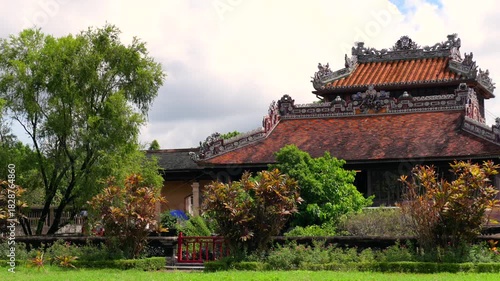 A wooden frame reveals the two-story Minh Lau Pavilion, perched on a rustic stone base amidst manicured geometric gardens