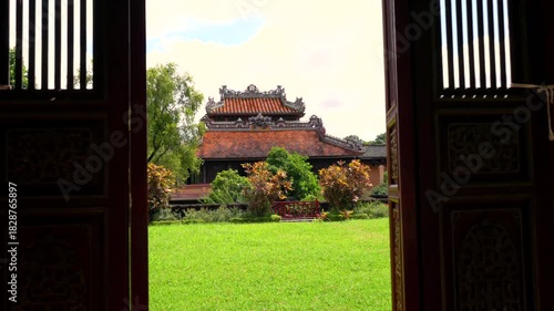 A wooden frame reveals the two-story Minh Lau Pavilion, perched on a rustic stone base amidst manicured geometric gardens
