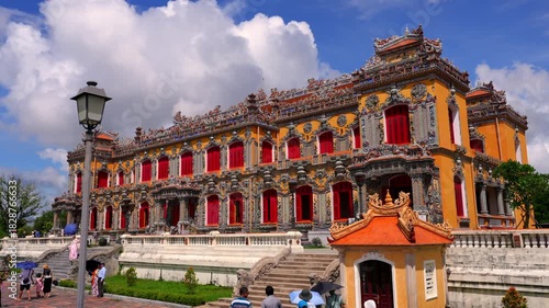 Majestic Kien Trung Palace featuring vibrant yellow walls, ornate ceramic mosaics, and striking red shutters against a cloudy blue sky.